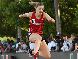 Female track member jumping over a hurdle.